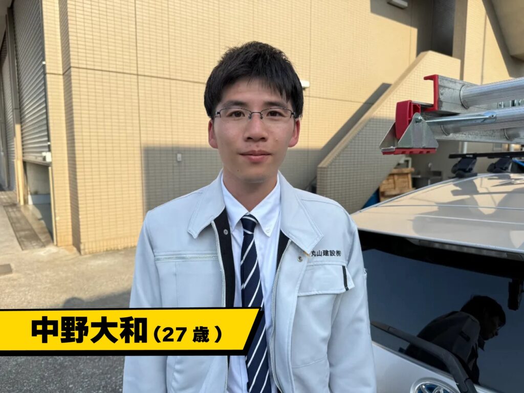 丸山建設株式会社の営業部長・中野大和が営業車の前で挨拶している様子