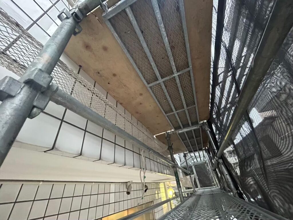 建物の入り口の仮設足場に、落下防止のコンパネを設置した写真