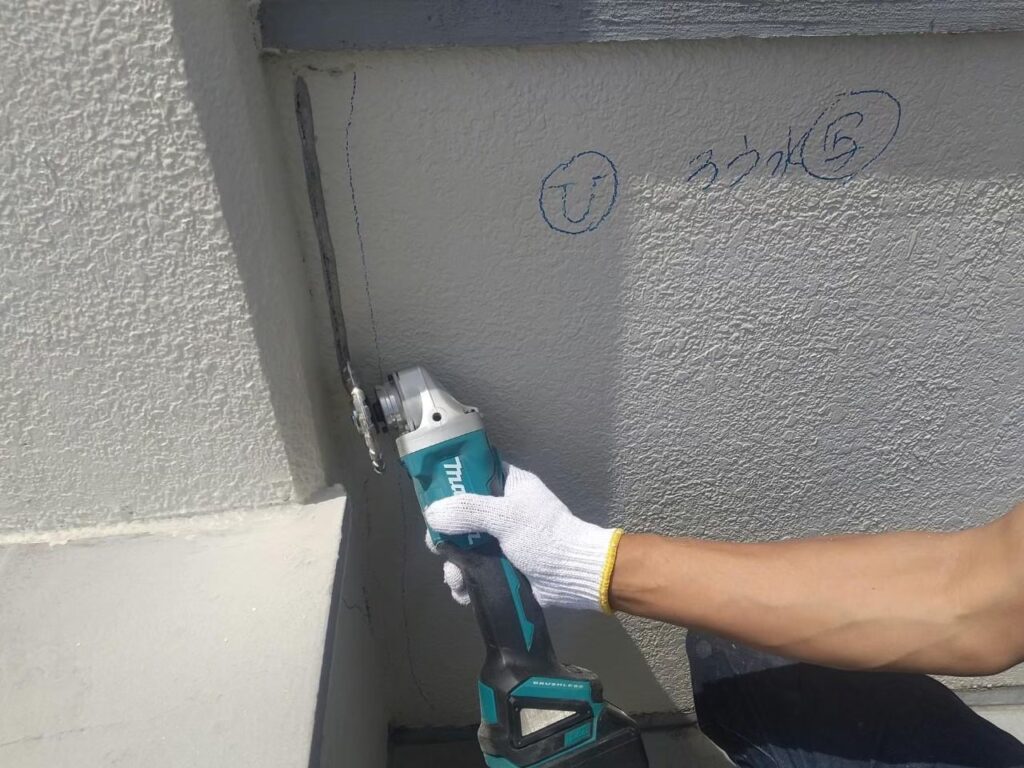 雨漏りの原因の外壁のひび割れ部分をサンダーでVカットしている写真