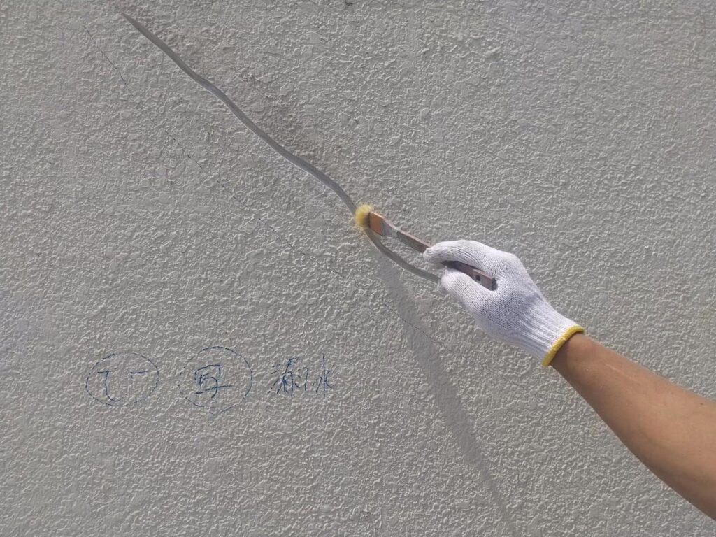 外壁のひび割れをサンダーでVカットした後に刷毛で埃を落としている写真