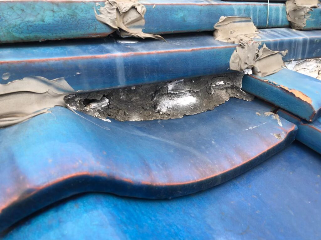 瓦屋根の棟部分で漆喰が腐食し、黒ずみや欠損が確認できる様子