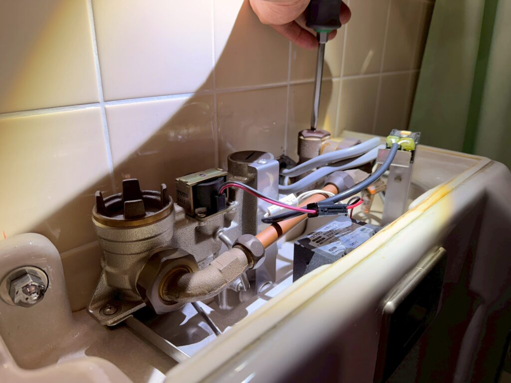 マイナスドライバーで電磁弁に設置されている止水栓を回しているが、劣化により止水栓が回らない写真