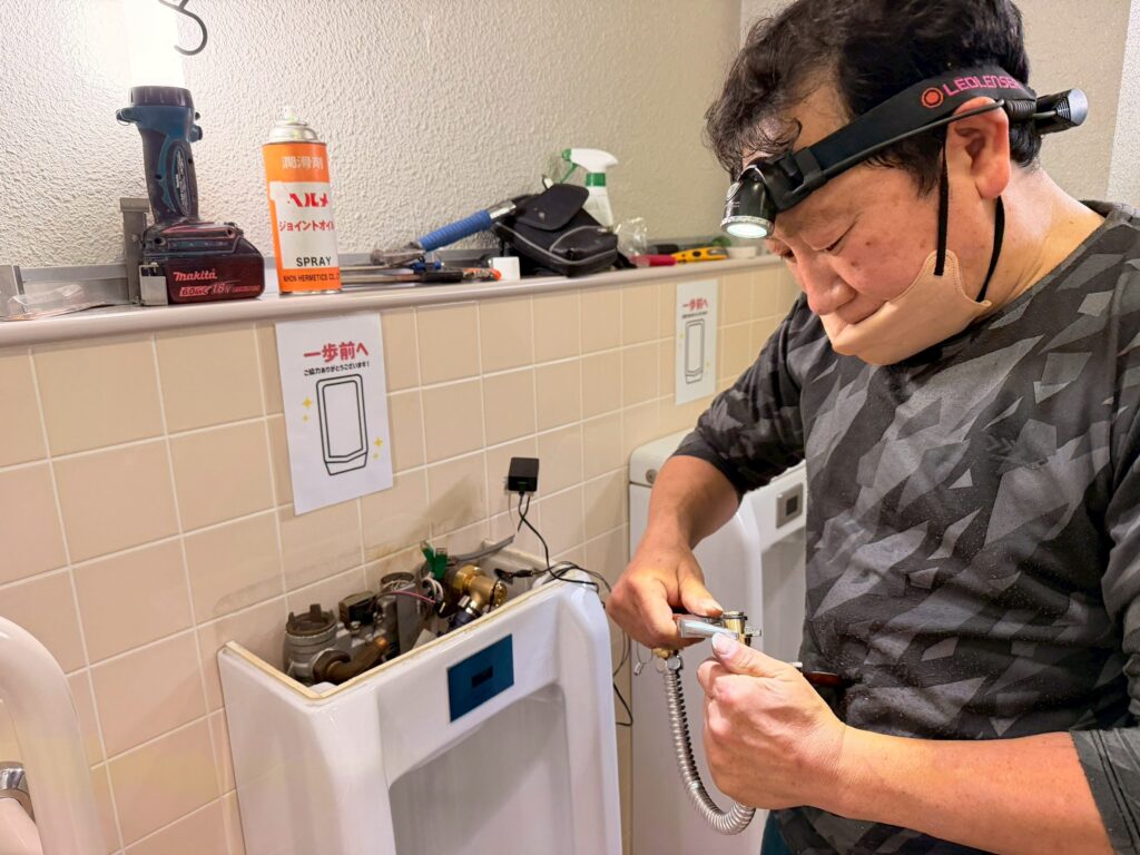丸山建設株式会社の設備担当の職人さんが、不要となった器具を撤去し新しい電磁弁とセンサーを取り付けている写真