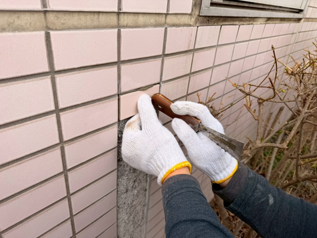 はじめの外壁タイル1枚目を、位置とバランスを微調整しながら貼り付けている写真