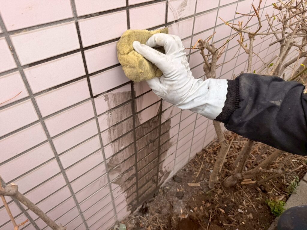新しい外壁タイルの表面に付着した余分な目地材や汚れを、専用のスポンジを使用して丁寧に洗浄している写真