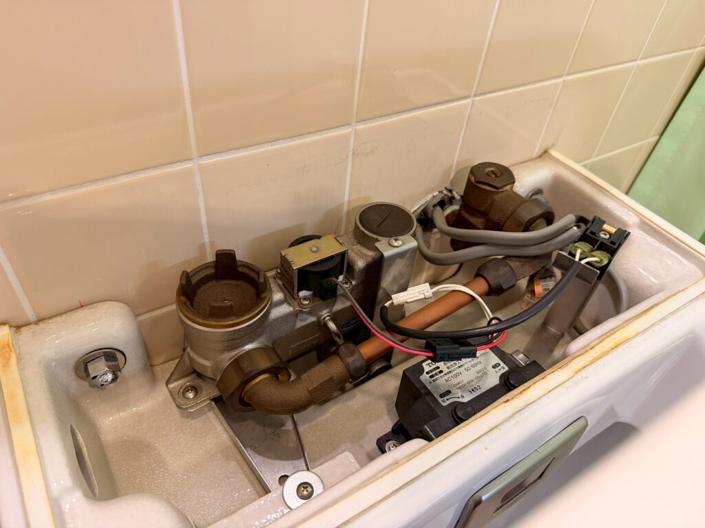 外来棟・療養病棟の男子トイレの便器上部のカバーを取り外し、TOTO製のセンサーと電磁弁が見えている写真
