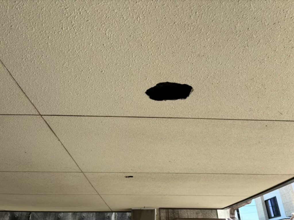 大きな穴が開き内部の木材が見えている軒天