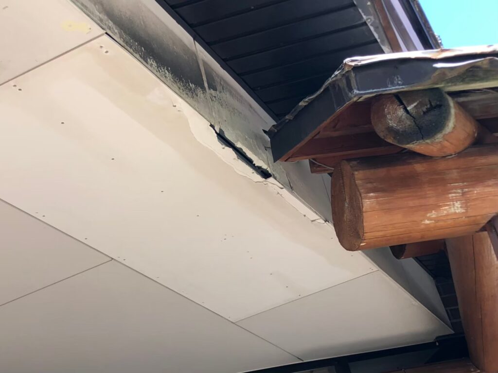 大きな穴が開き内部の木材が見えている軒天